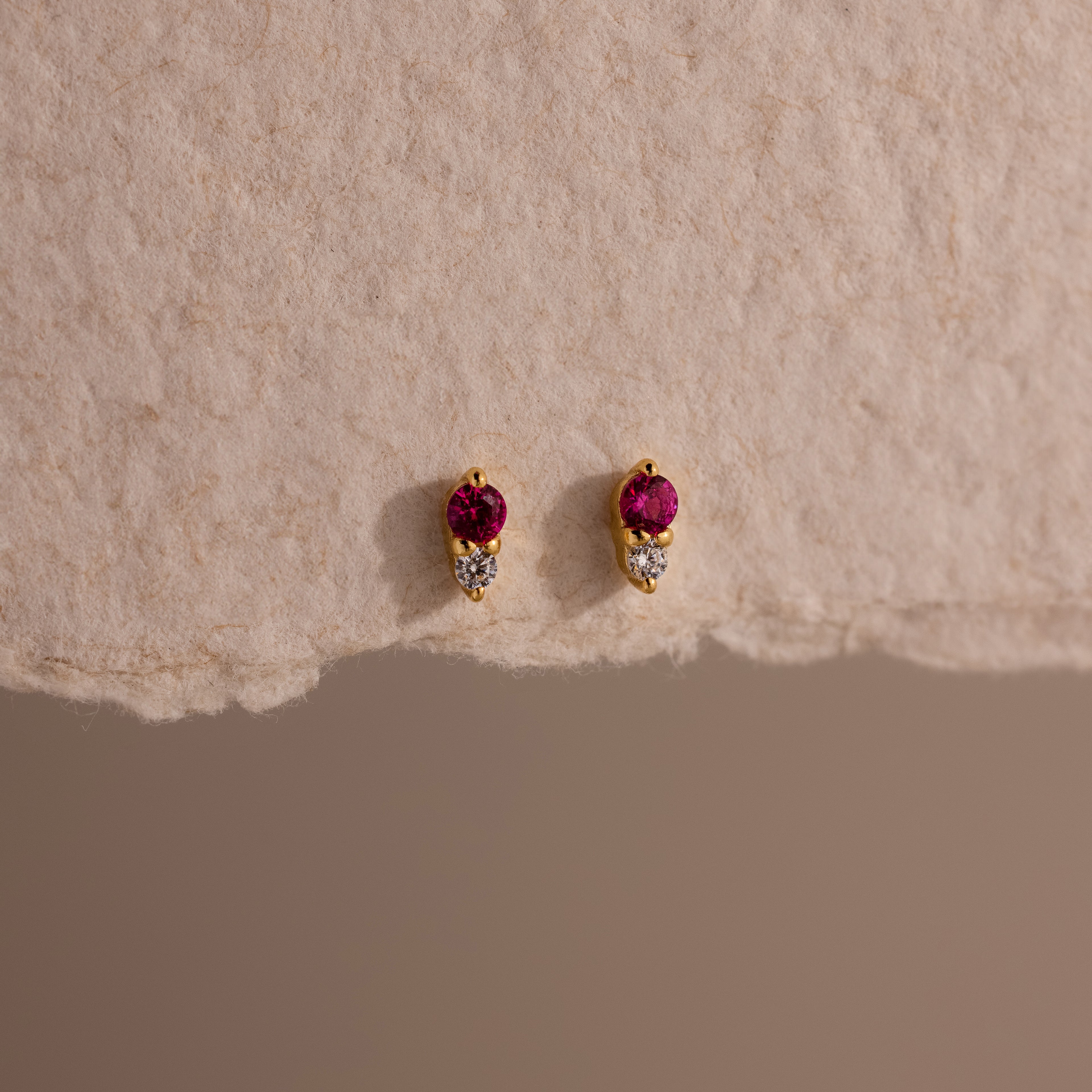 Tiny Duo Ruby Flatback Studs featuring small red and clear stones, displayed on textured beige paper.