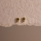 Tiny Duo Peridot Flatback Studs—gold earrings featuring green peridot stones and diamond accents, shown on a textured beige surface—perfect for adding an elegant touch to your ear stack.