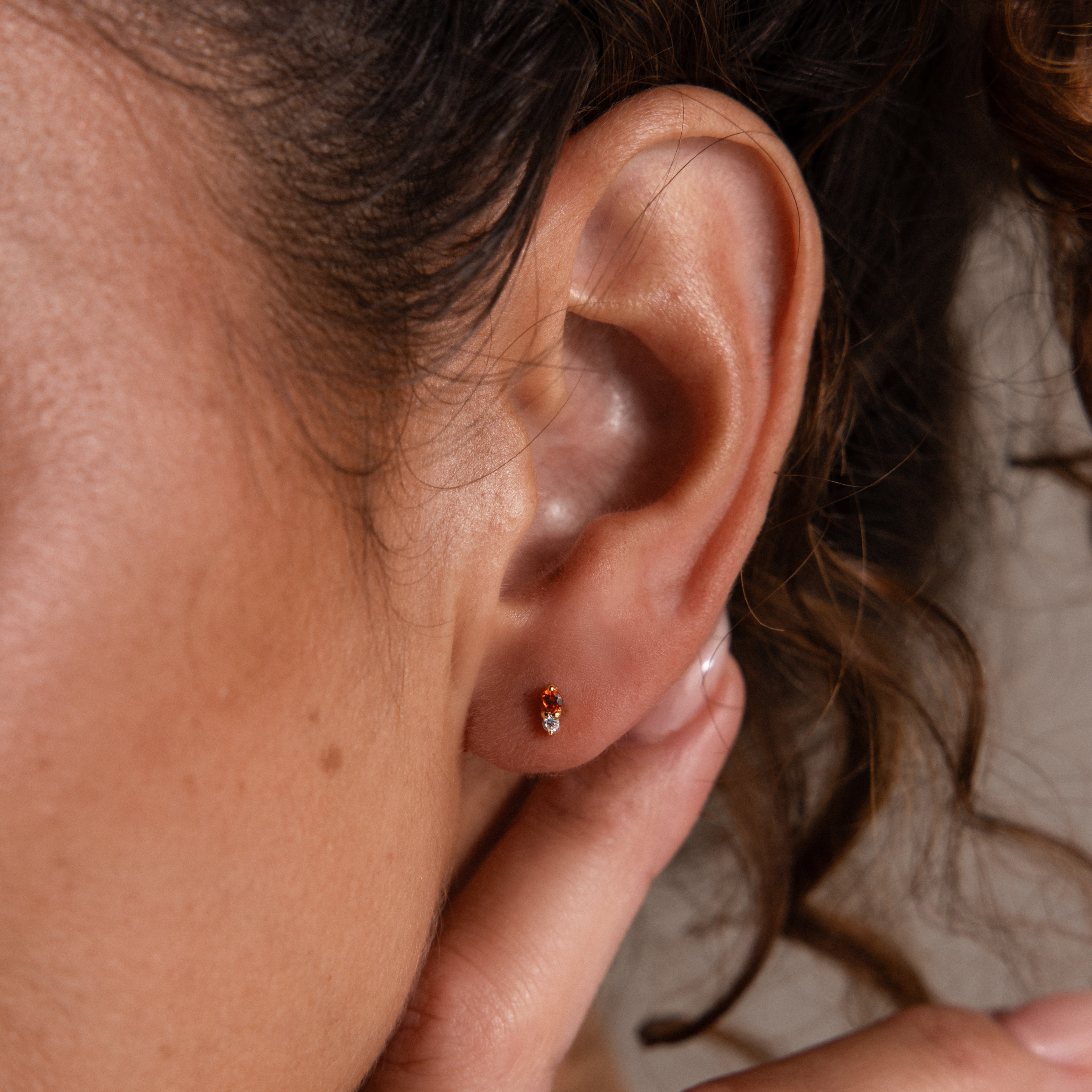 Close-up of a woman’s ear adorned with Tiny Duo Topaz Flatback Studs, her hand gently touching her earlobe.