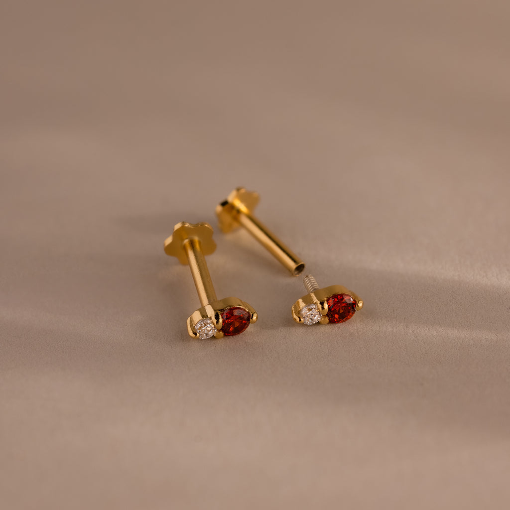 The Tiny Duo Birthstone Flatback Studs, crafted in gold with red and clear gemstones, bring elegance to any look. These dazzling birthstone studs beautifully enhance even the most neutral styles.