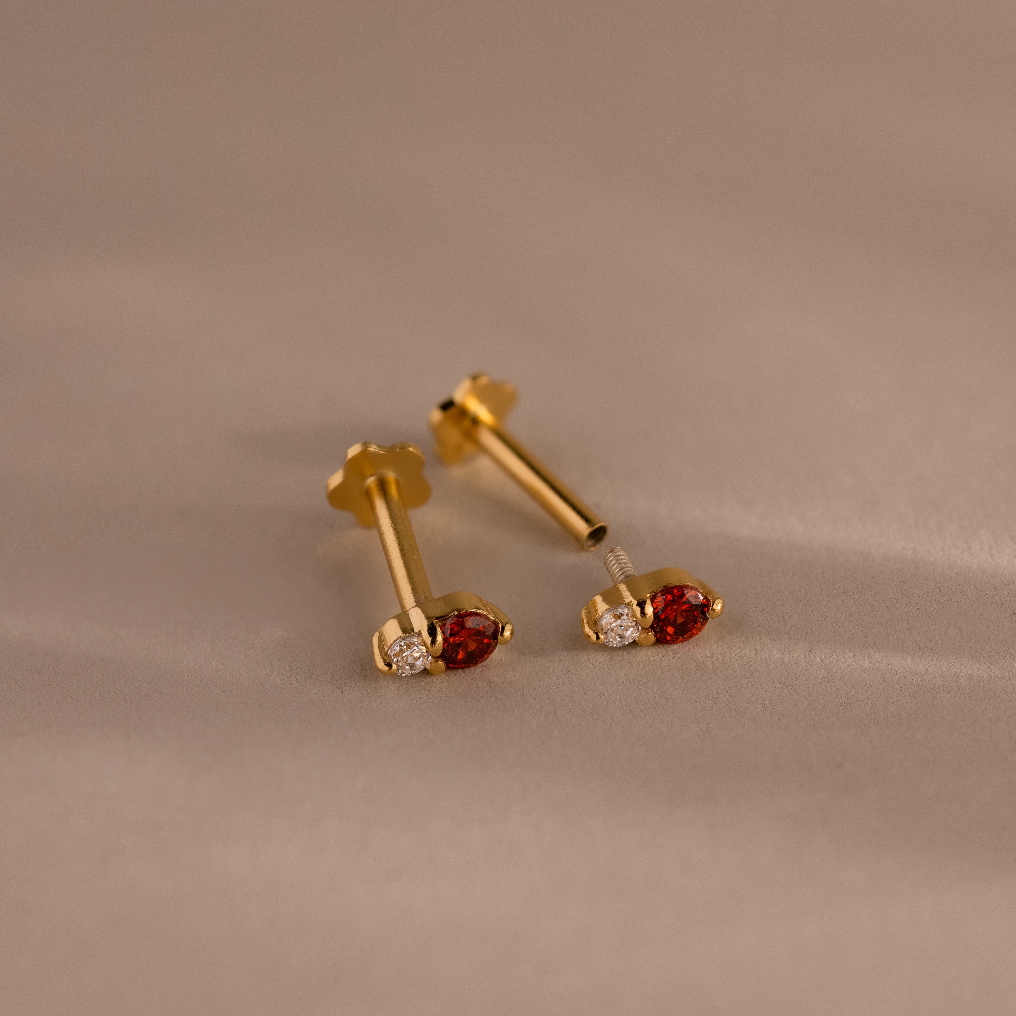 The Tiny Duo Birthstone Flatback Studs, crafted in gold with red and clear gemstones, bring elegance to any look. These dazzling birthstone studs beautifully enhance even the most neutral styles.