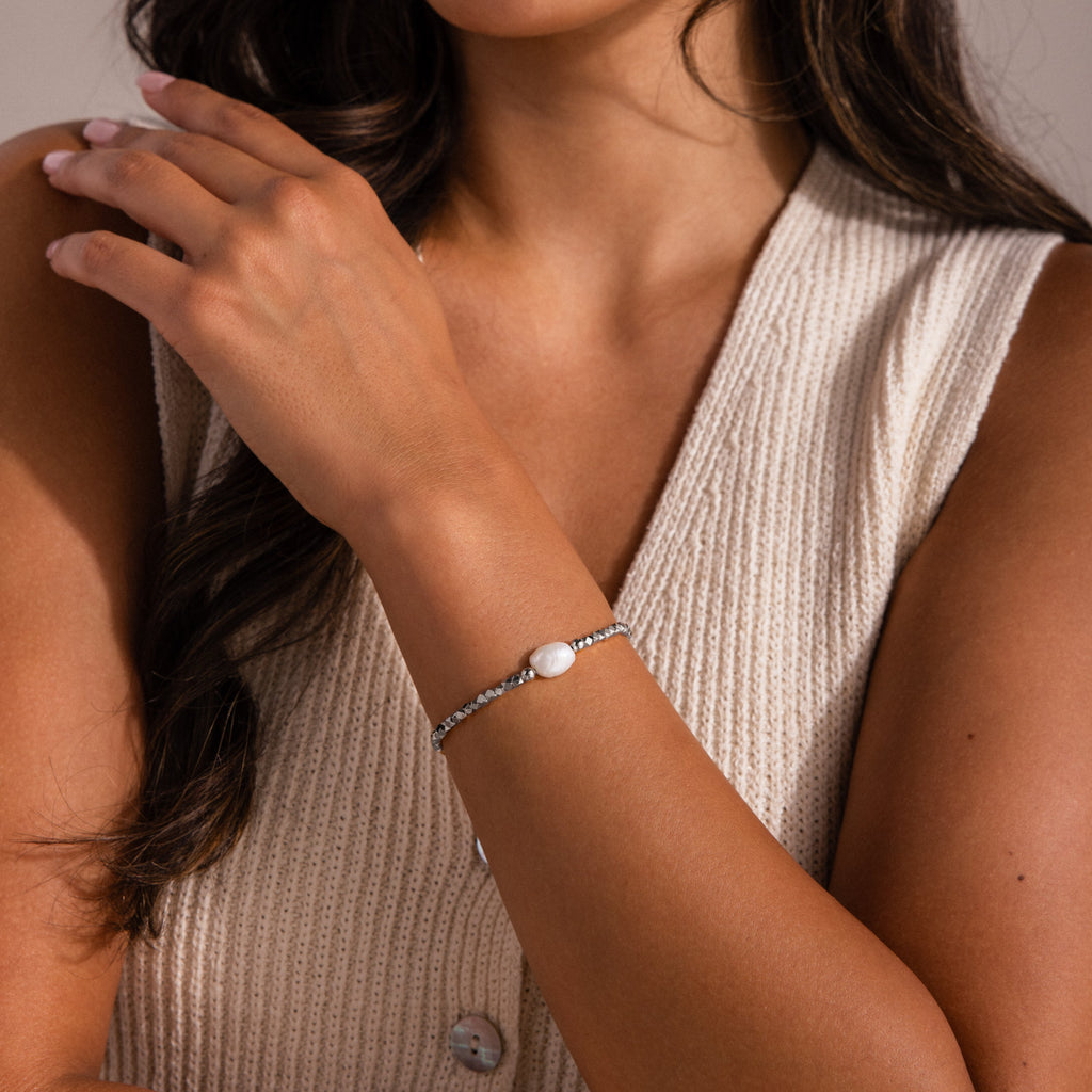 Model wearing a silver beaded bracelet featuring a single white coin pearl, styled with a cream knit sleeveless top.
