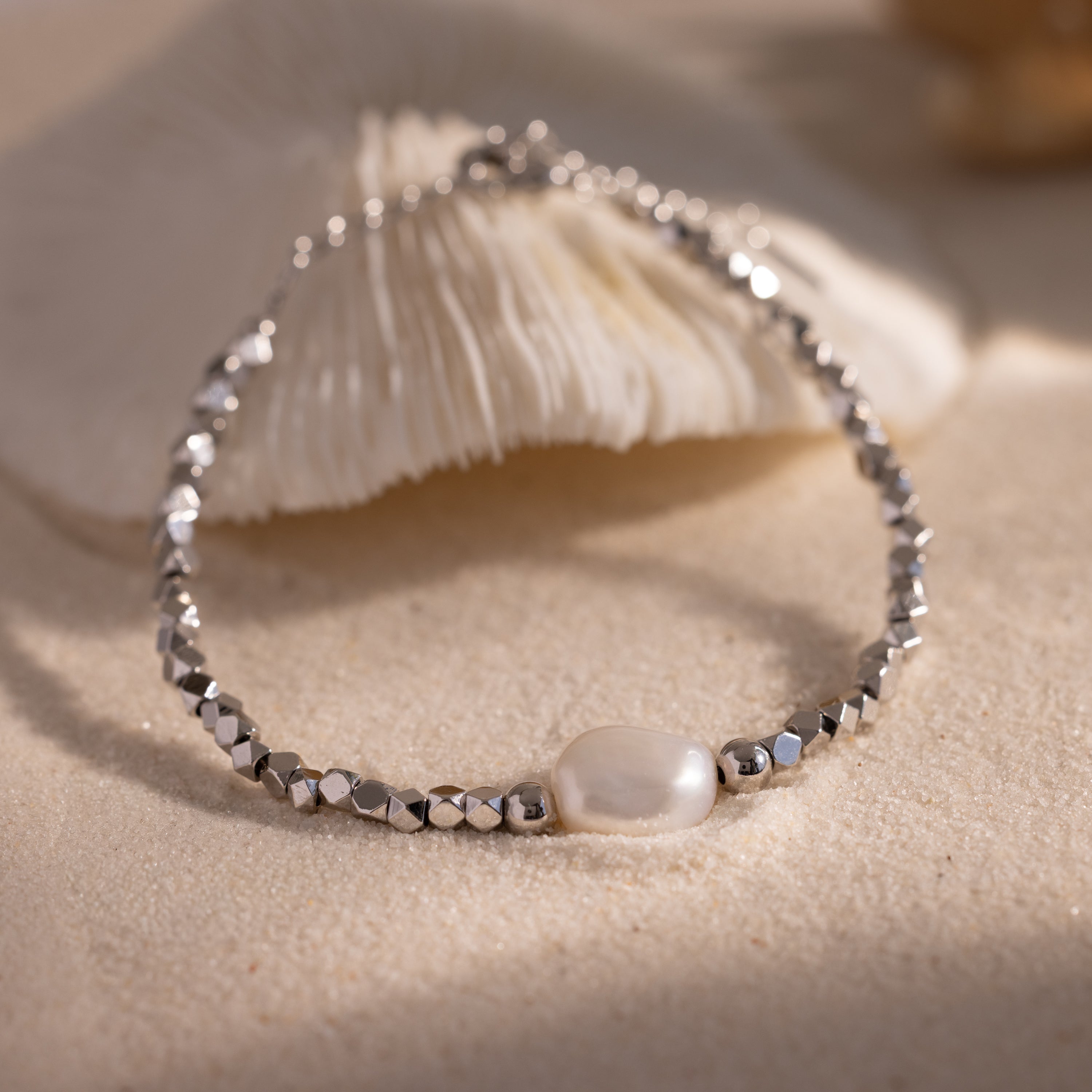 Beaded Pearl Bracelet crafted with faceted silver beads and accented by a single natural white pearl centerpiece, displayed on a sandy surface for a refined, coastal inspired look.