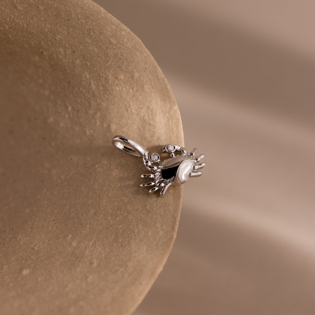 Silver crab charm pendant with gemstone eyes, displayed on a soft neutral background.