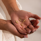 Hand holding five small gold charms, including a pavé seashell charm, a shark tooth, a fish, a lion head, and a sea creature charm, all finely detailed and glinting under soft light.