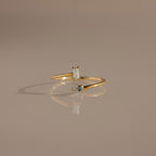 The Toi et Moi Wrap Ring in 18K Gold features two small opal stones and is displayed on a neutral beige surface.