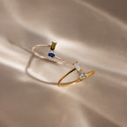A Toi et Moi Wrap Ring in Silver with delicate gemstones is displayed on a softly lit beige surface.