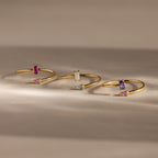 The Toi et Moi Wrap Ring in 18K Gold features delicate overlapping bands adorned with vibrant rectangular and teardrop gemstones, elegantly displayed on a neutral background.