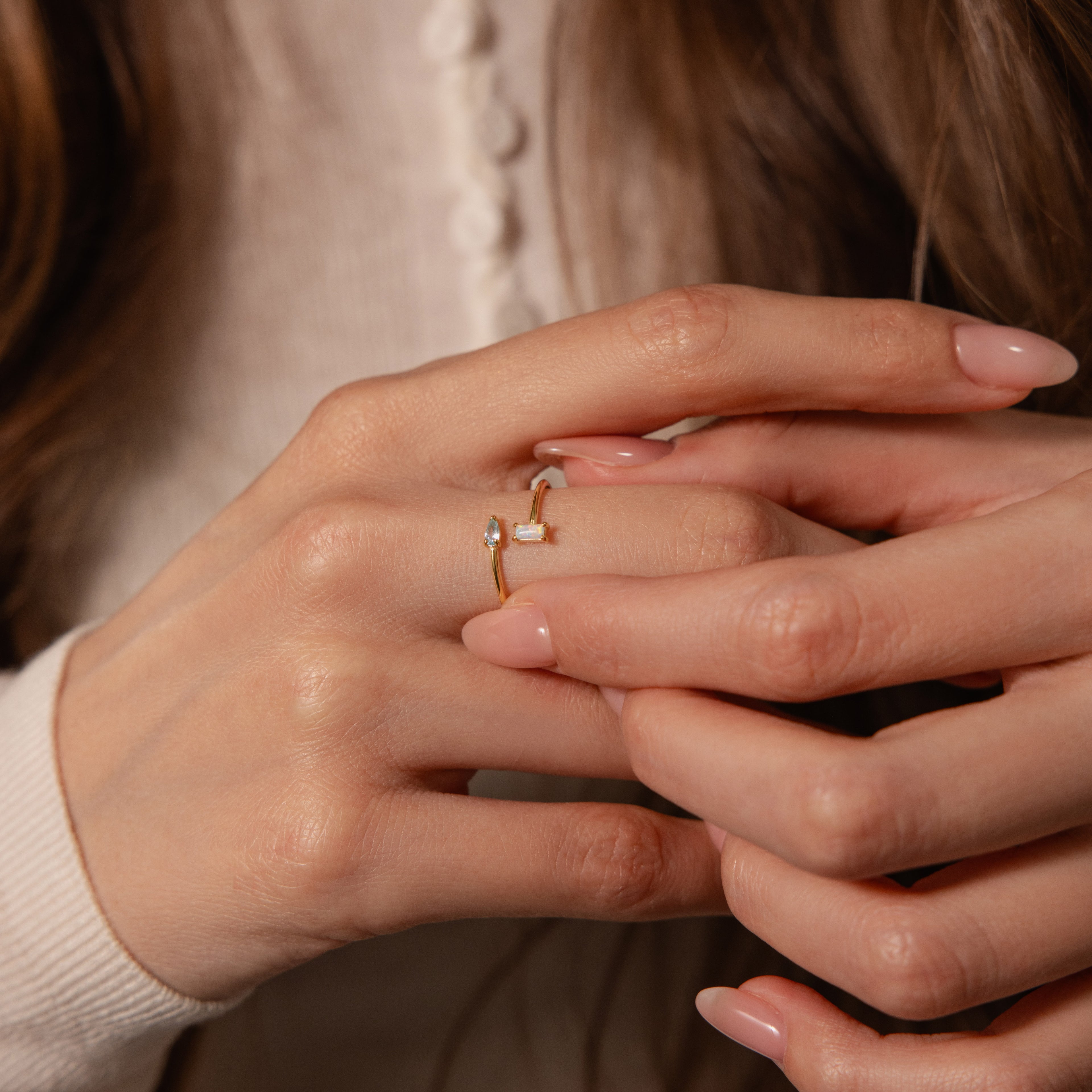 Close-up of manicured hands wearing the Toi et Moi Wrap Ring, a gold stacking ring with a small clear stone on the middle finger.