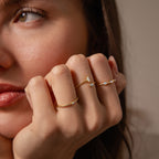 A woman’s face in soft focus highlights her fingers adorned with the Toi et Moi Wrap Ring, showcasing its elegant, delicate gold design up close.