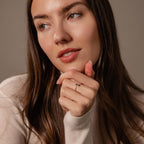 Woman with long brown hair, dressed in a beige top, looks to the side and rests her chin on her hand, highlighting the Toi et Moi Wrap Ring in Silver for a romantic touch to her elegant look.