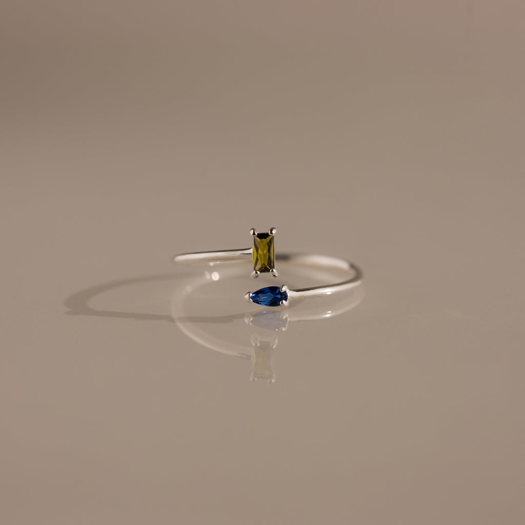 The Toi et Moi Wrap Ring in Silver showcases a minimalist design with a yellow rectangular and blue teardrop gemstone, displayed on a neutral background.
