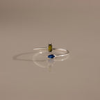 The Toi et Moi Wrap Ring in Silver showcases a minimalist design with a yellow rectangular and blue teardrop gemstone, displayed on a neutral background.