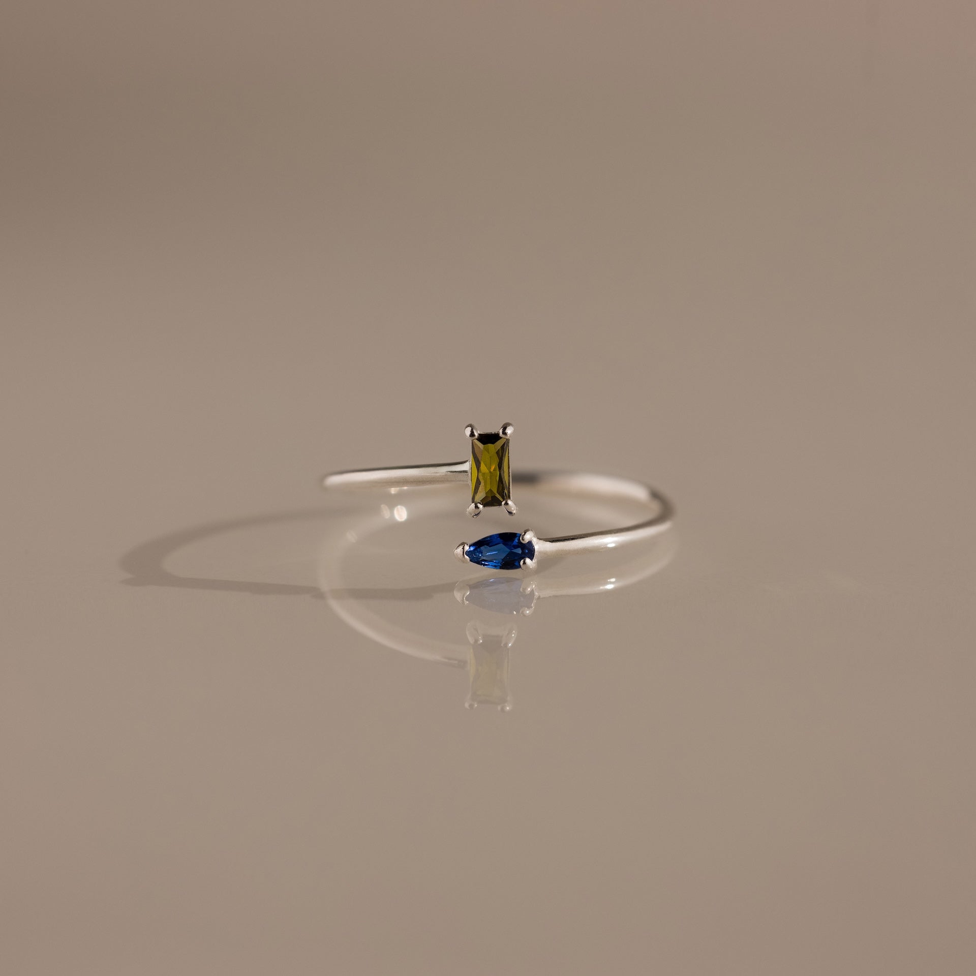 The Toi et Moi Wrap Ring features a rectangular yellow gemstone and a marquise blue gemstone set in silver, displayed on a neutral background—a timeless romantic jewelry piece.