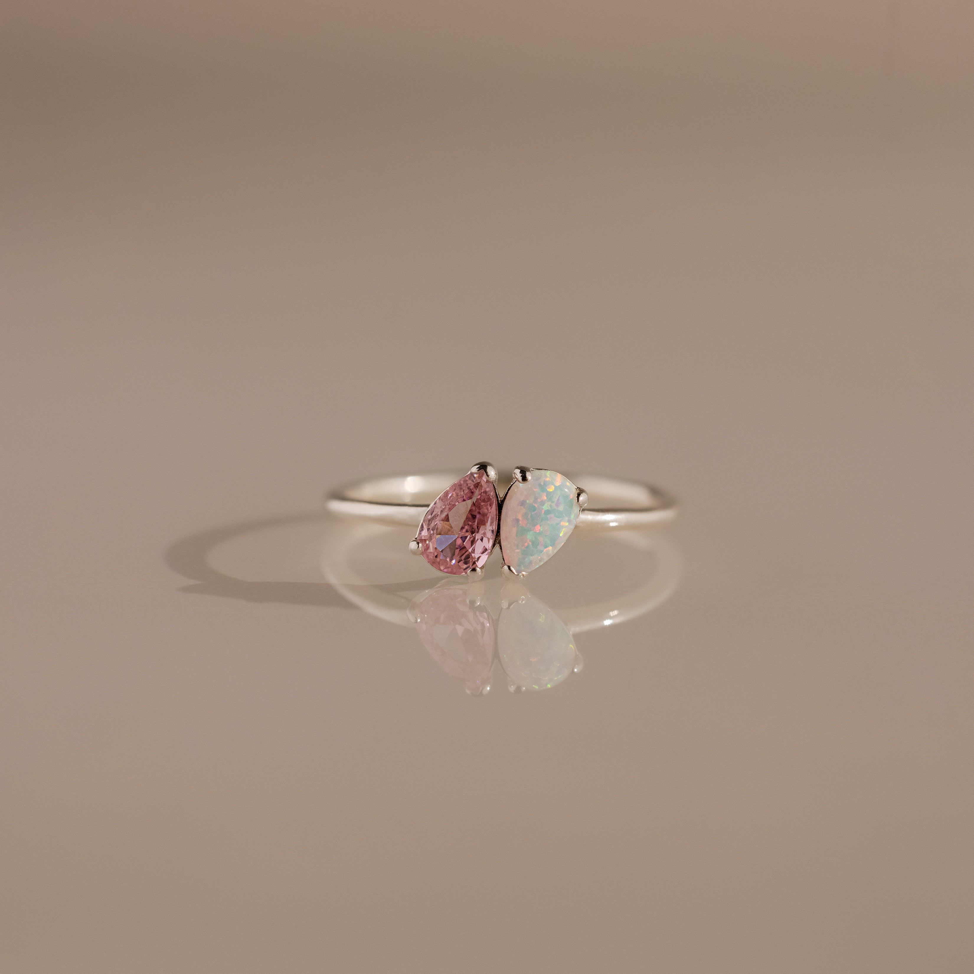 The Duo Pear Toi Et Moi Ring in Silver showcases a romantic design with pear-shaped pink and iridescent gemstones, set in silver and elegantly displayed on a neutral background with a soft shadow.