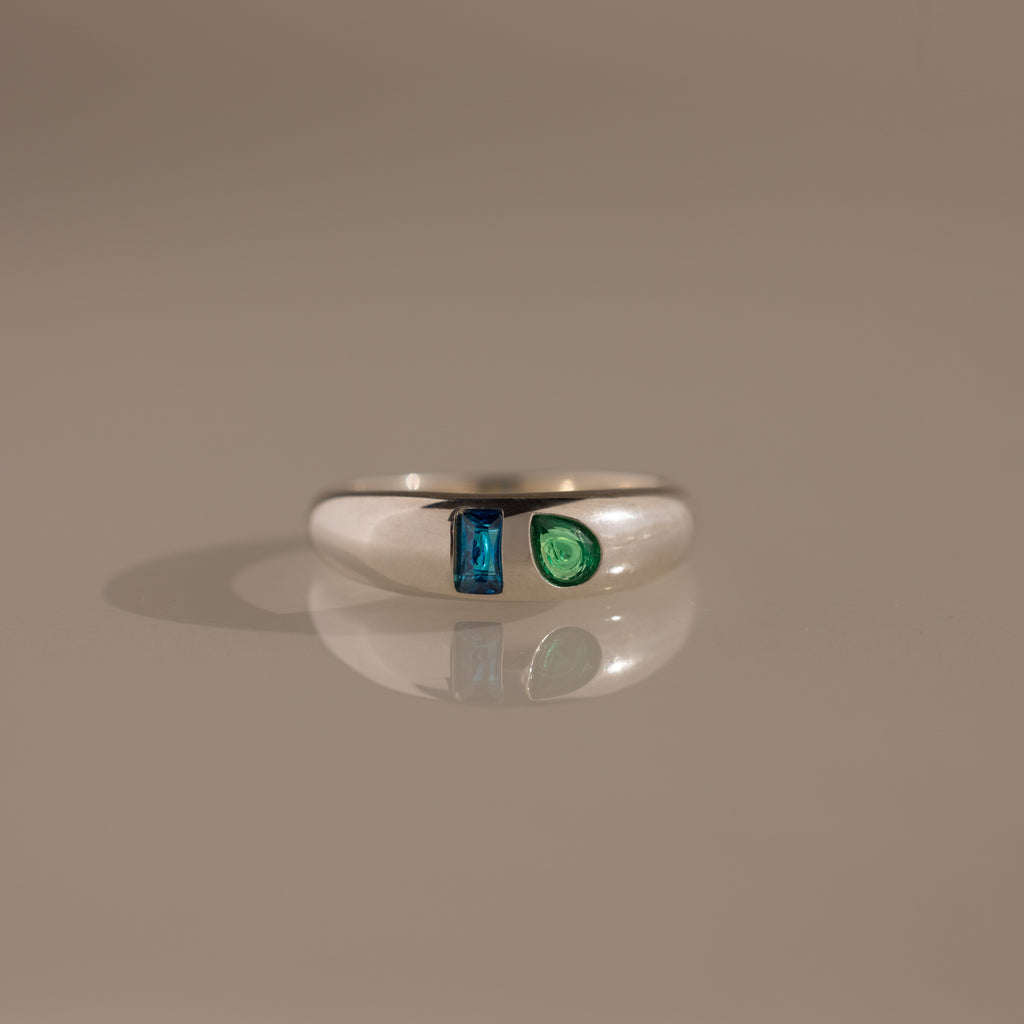 The Toi et Moi Dome Ring in Silver showcases a blue rectangular gem and a green teardrop-shaped gem set side by side.