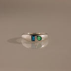 The Toi et Moi Dome Ring in Silver showcases a blue rectangular gem and a green teardrop-shaped gem set side by side.