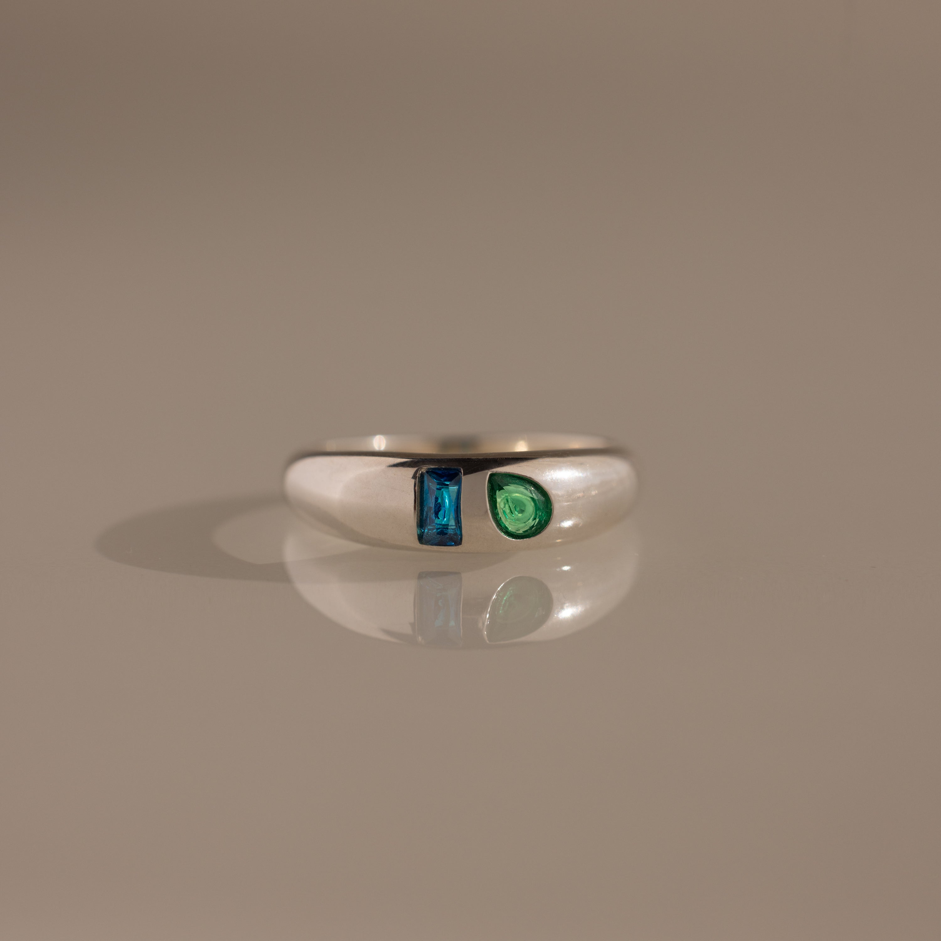 The Toi et Moi Dome Ring in Silver showcases a blue rectangular gem and a green teardrop-shaped gem set side by side.