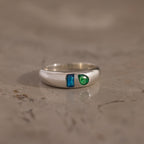 The Toi et Moi Dome Ring in Silver features a blue rectangular gem and a green round gem, displayed on a marble surface.