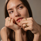 A woman with long brown hair, wearing the Toi et Moi Dome Ring in 18K Gold, rests her face on her hands and gazes slightly to the side.