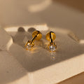 A pair of Diamond Flatback Studs with clear gemstones displayed on a textured beige surface.