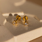 A pair of Diamond Flatback Studs with clear gemstones displayed on a textured beige surface.