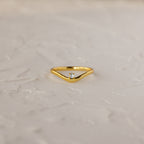 The Diamond Drop Curve Ring features a V-shaped gold band with a small central diamond, displayed on a textured light surface.