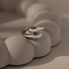 The Duo Dome Ring in White Gold, featuring a modern adjustable band, rests on a textured light beige sculptural surface, epitomizing contemporary sculptural jewelry.