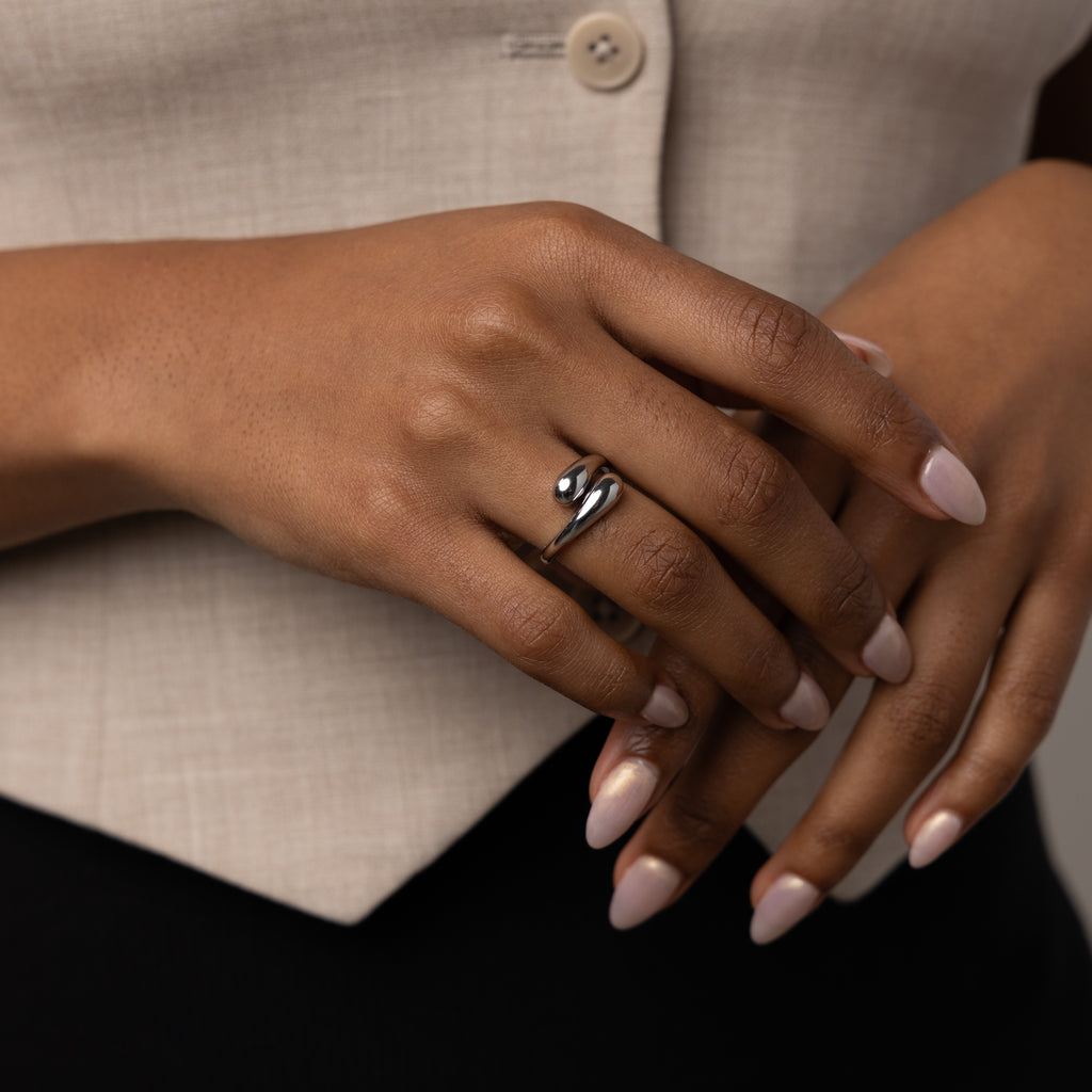 A hand with manicured nails wears the Duo Dome Ring featuring an adjustable band; the person is dressed in a beige top and black pants.