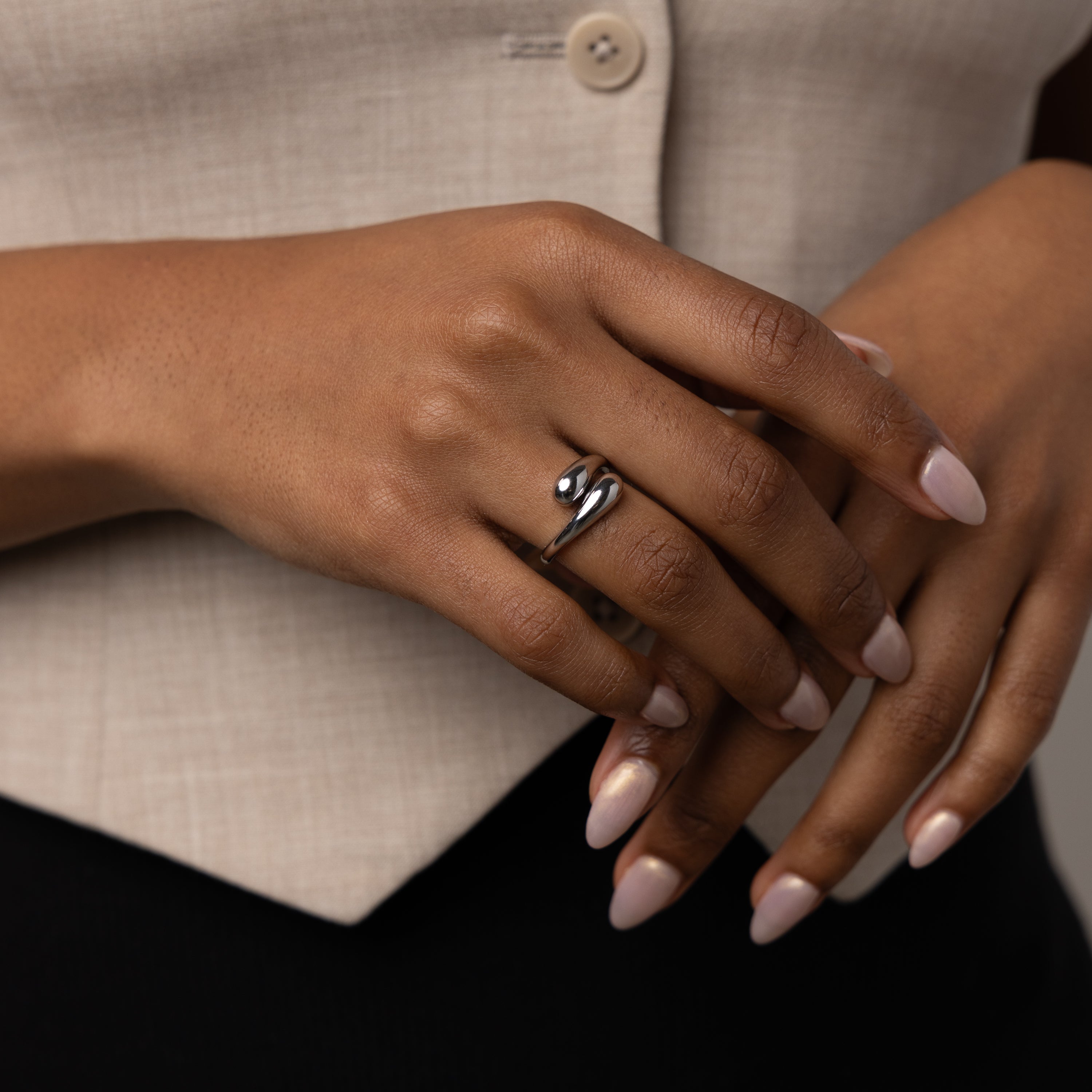 A hand with manicured nails wears the Duo Dome Ring featuring an adjustable band; the person is dressed in a beige top and black pants.
