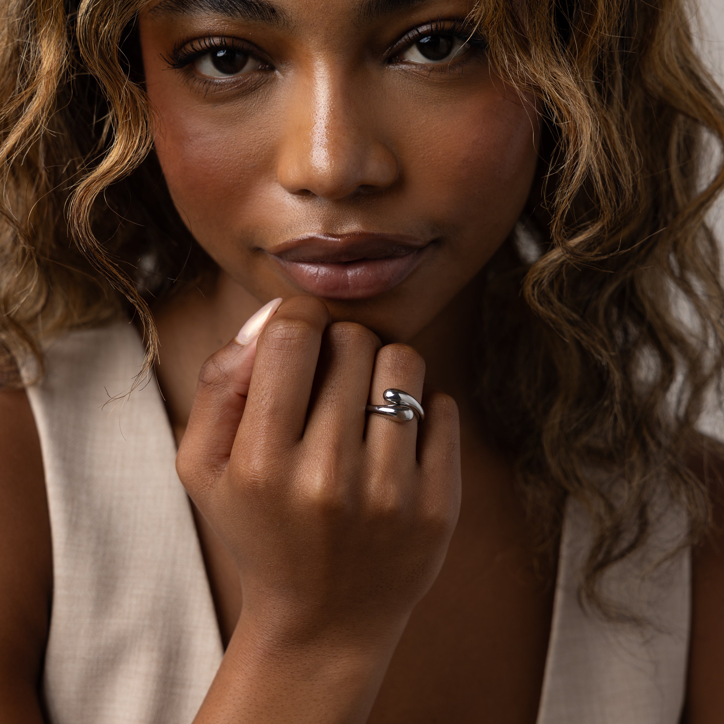 Woman with wavy hair poses, wearing a beige top and the Duo Dome Ring in White Gold with an adjustable band on her finger, looking at the camera.