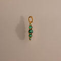 A gold Ombre Lace Emerald Charm with four stacked green beads on a plain beige background.