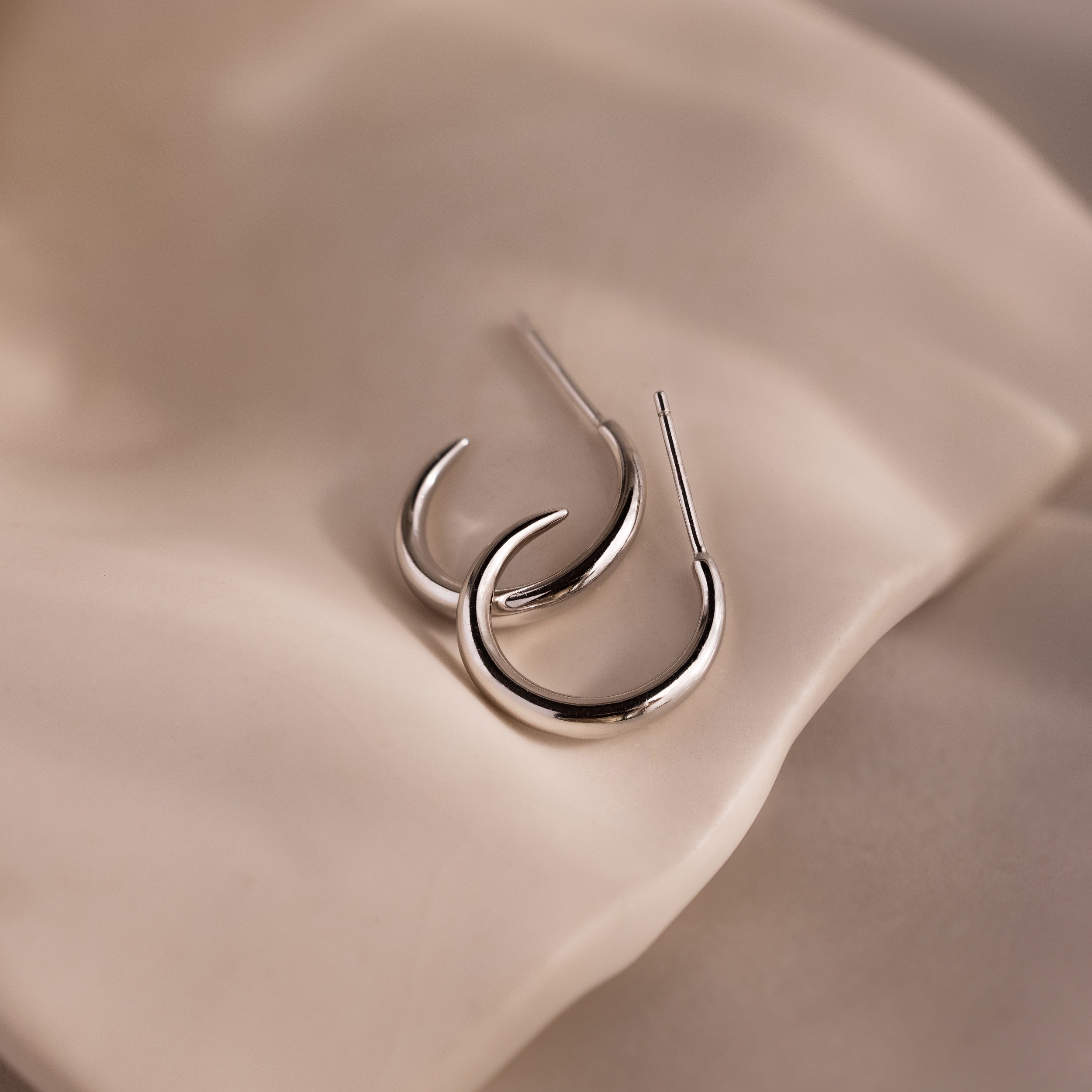 Silver stud hoop earrings on a beige stone background