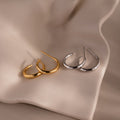 Gold and silver hoop stud earrings on a beige fabric background