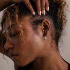 Close-up of a woman with silver hoop stud earrings, curly hair, and a hand touching her head