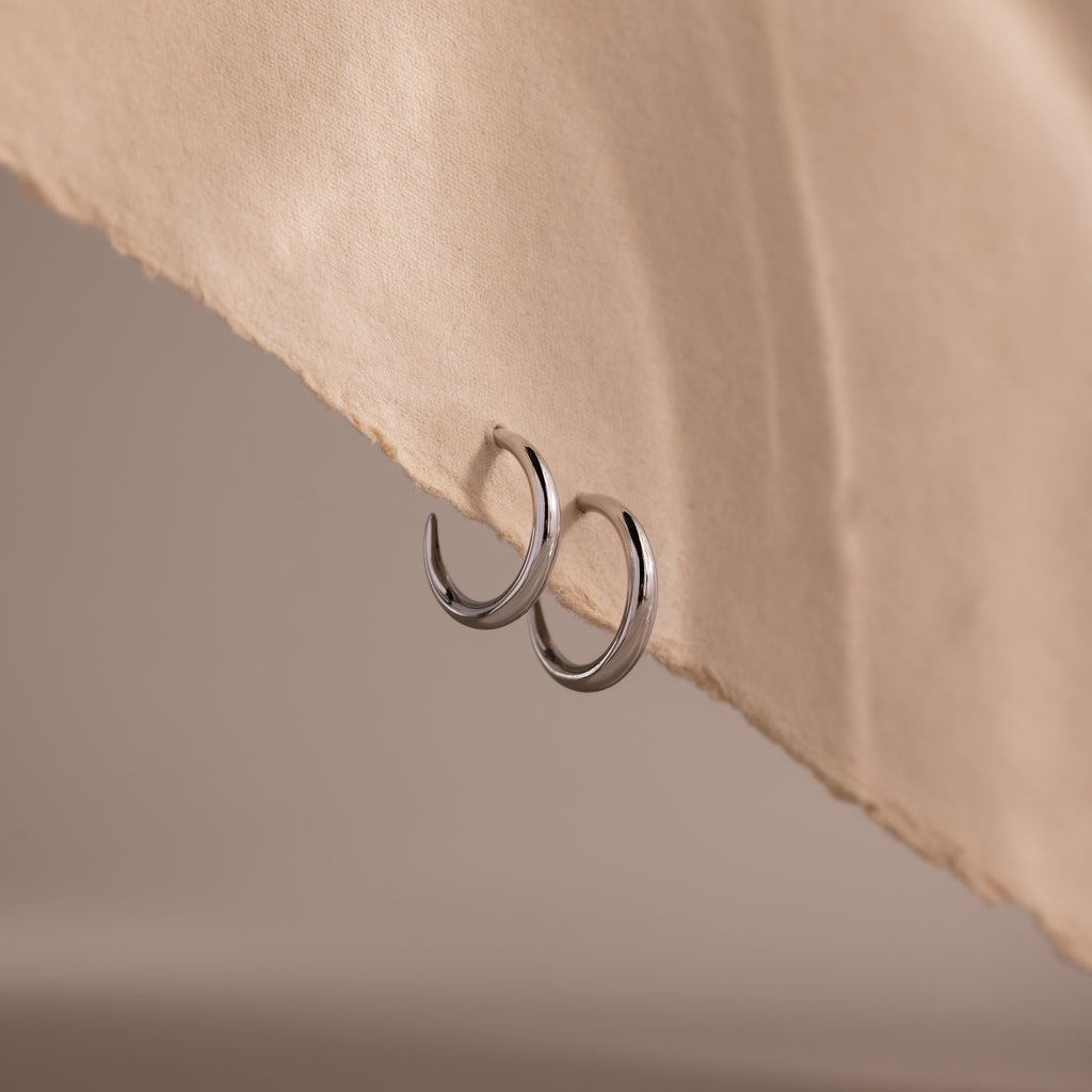 Silver stud hoop earrings on a beige fabric background