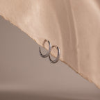 Silver stud hoop earrings on a beige fabric background