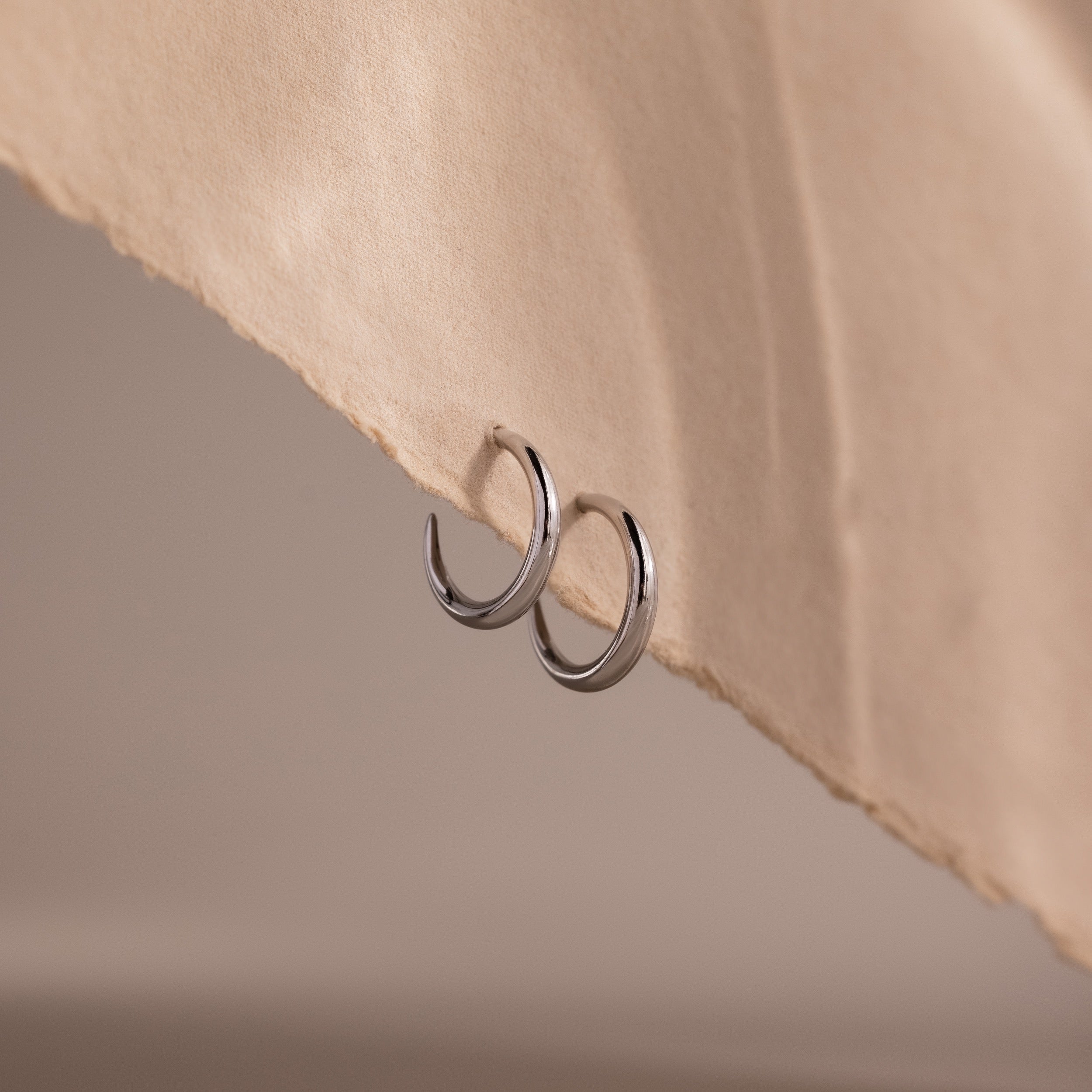 Silver stud hoop earrings on a beige fabric background