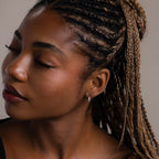 Close-up of a woman with braided hair and a silver hoop earring against a neutral background
