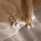 Pair of gold and silver hoop earrings with pearl drops on a beige fabric background 