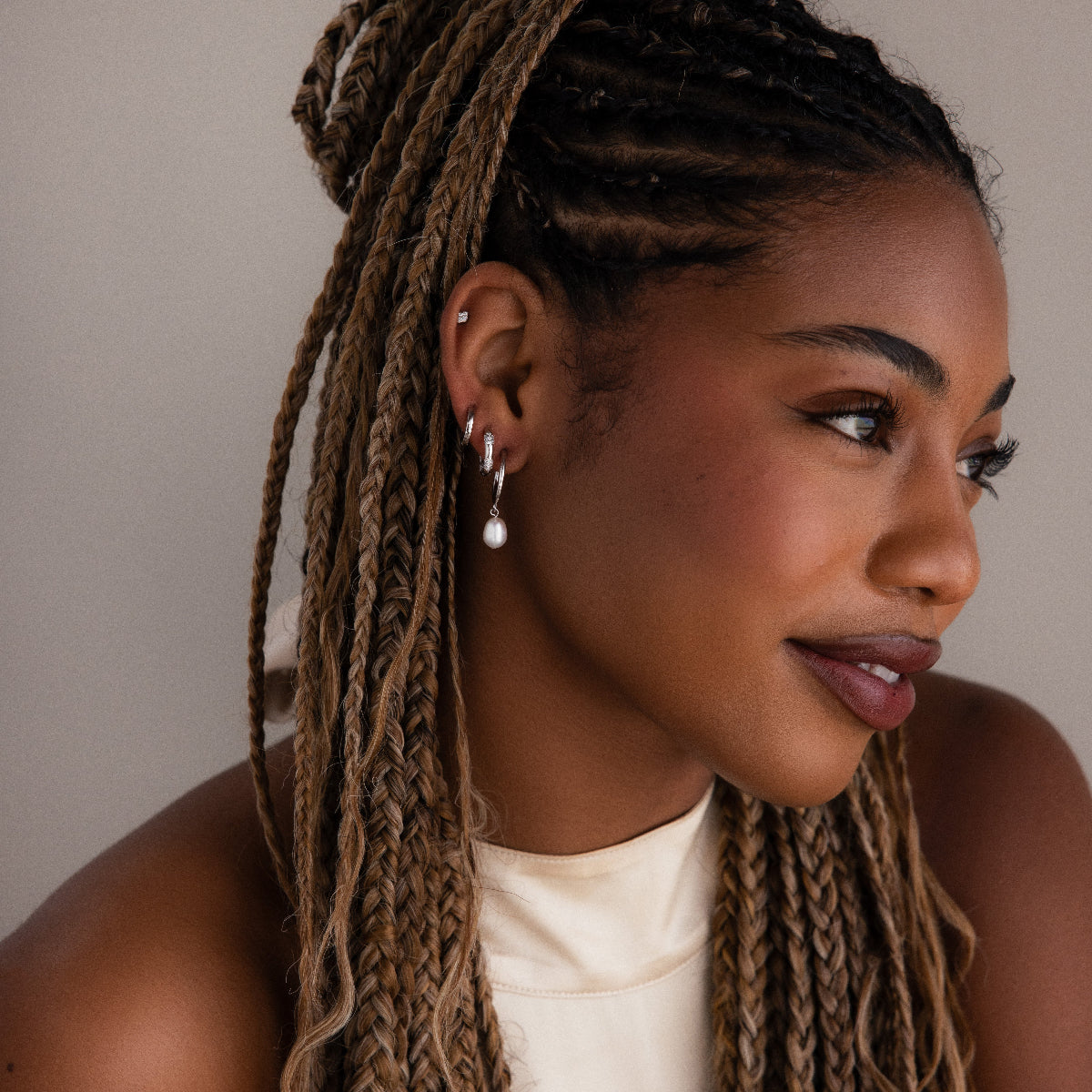 Woman with braided hair wearing various silver earrings against a neutral background