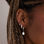 Close-up of a model with multiple silver earrings and braided hair against a neutral background