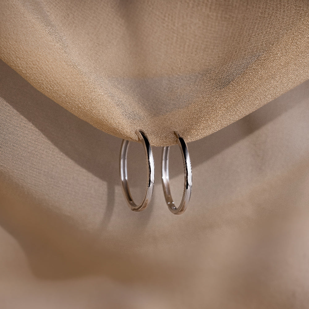Two silver hoop earrings on a beige fabric background