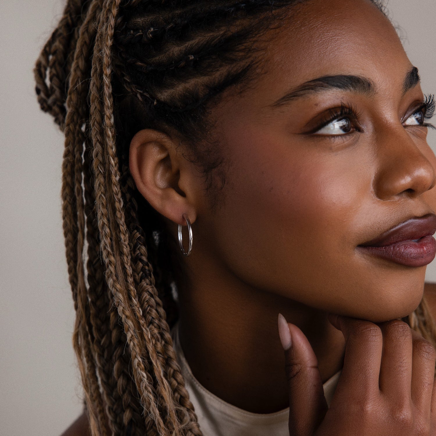 Woman with braided hair and a silver hoop earring touching her chin against a neutral background