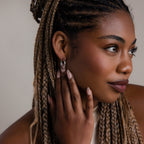 Woman with braided hair touching her ear, wearing silver hoop earrings.