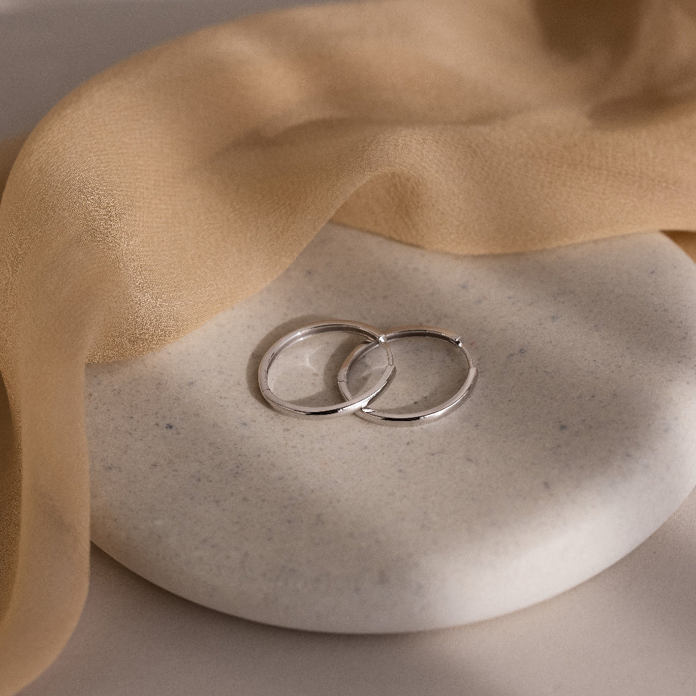 Two silver hoop earrings on a textured stone surface with beige fabric.