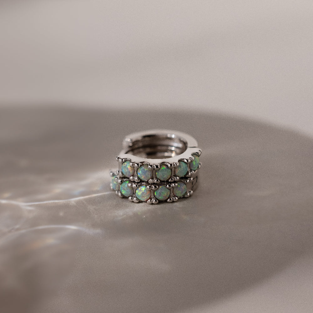 Silver huggie earrings with opal stones on a reflective surface