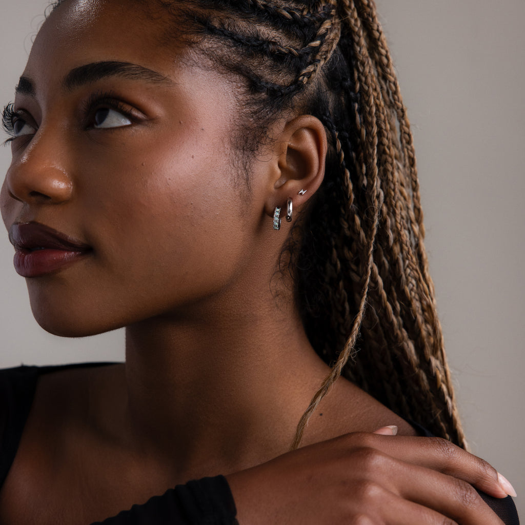 Woman with braided hair wearing multiple silver earrings against a neutral background