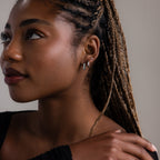 Woman with braided hair wearing multiple silver earrings against a neutral background