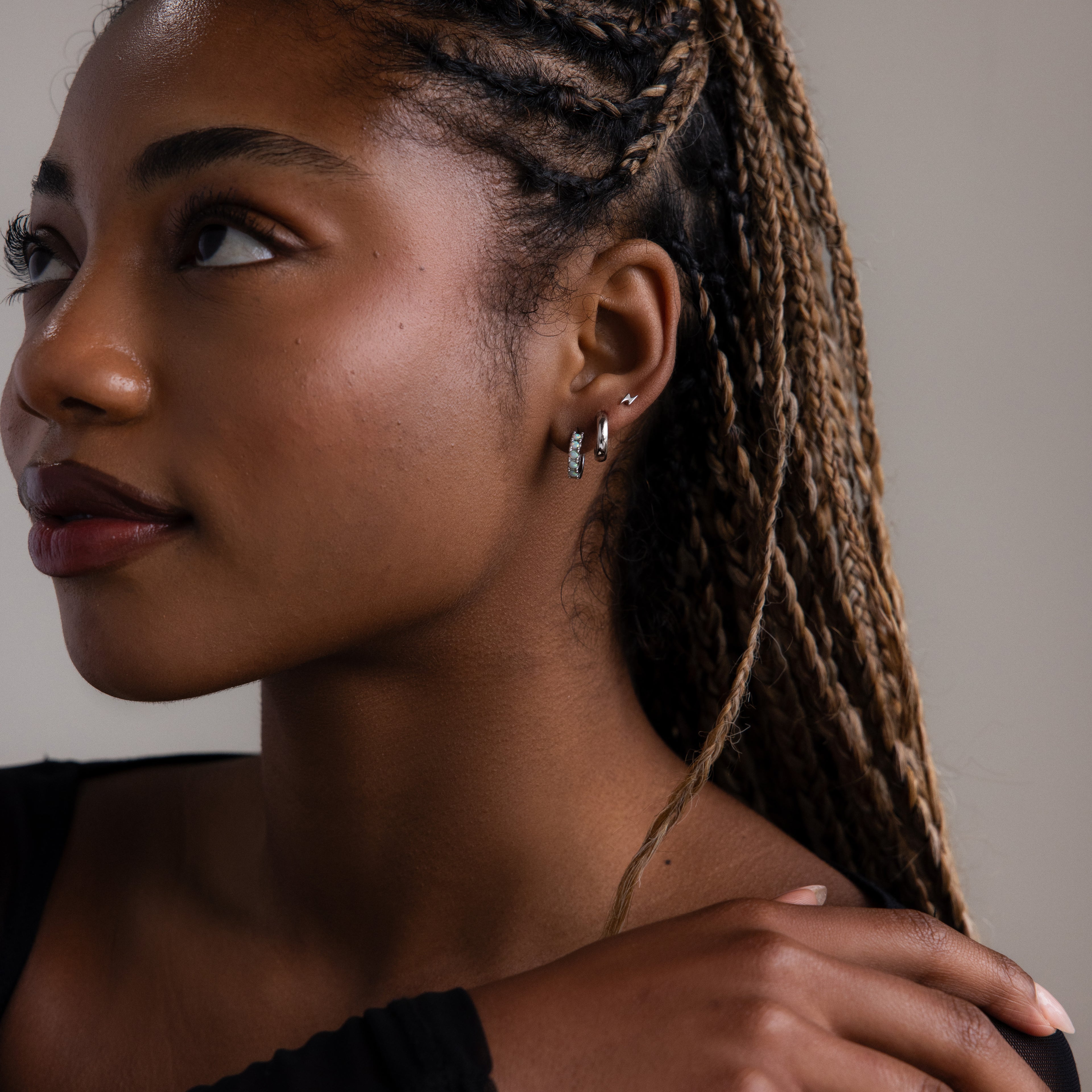 Woman with braided hair wearing multiple silver earrings against a neutral background
